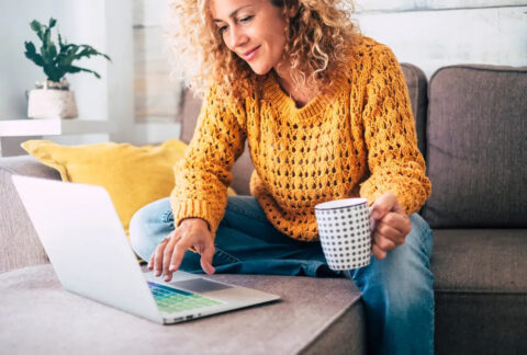 Woman sitting on sofa using laptop and holding a mug