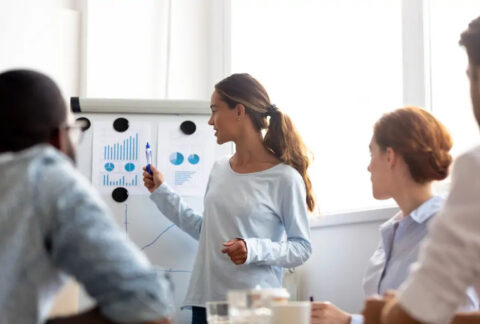 Businesswoman explaining charts and graphs on board to colleagues at meeting
