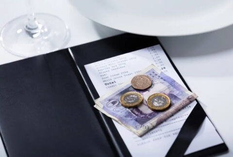 twenty pound note and three coins on top of a restaurant bill on table