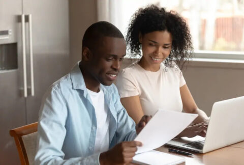 Couple sitting at table with laptop and documents looking at Income Tax