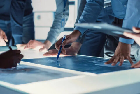 Businesspeople standing around illuminated table looking at R&D plans in a meeting