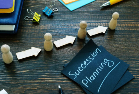 Wooden figurines in a row with arrows in between them next to a post-it note with 'succession planning' written on it