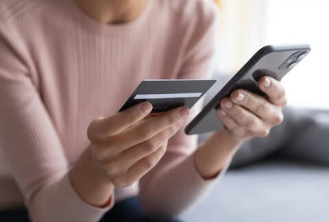 Woman sitting on sofa holding up bank card next to smartphone