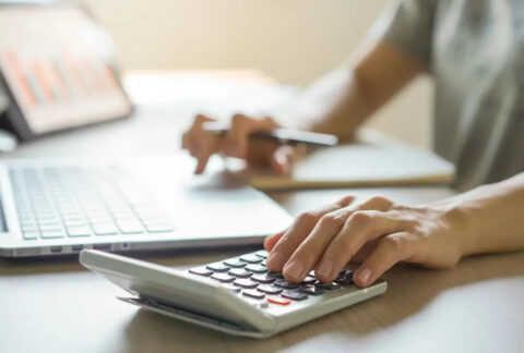 Woman using calculator with one hand and laptop with the other