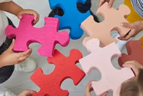 Five people standing in circle each holding a giant jigsaw piece in the middle