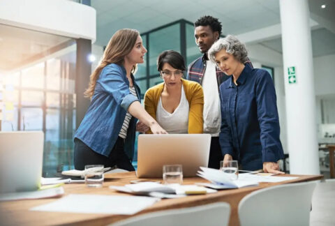 Team of colleagues gathered around desk looking at laptop