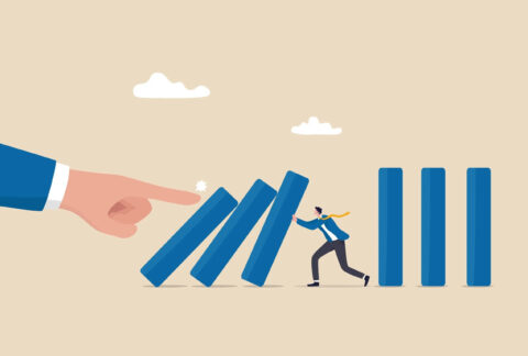 Cartoon of miniature businessman holding up toppling book spine-like rectangles that a giant finger has pushed over, with three more rectangles standing upright behind him
