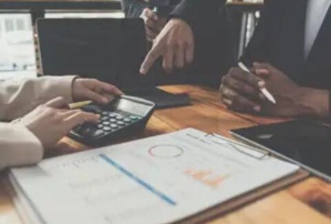 Businesspeople around table with calculator and printed documents calculating Corporation Tax