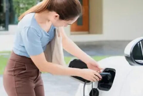 Woman connecting charger to electric car outside house