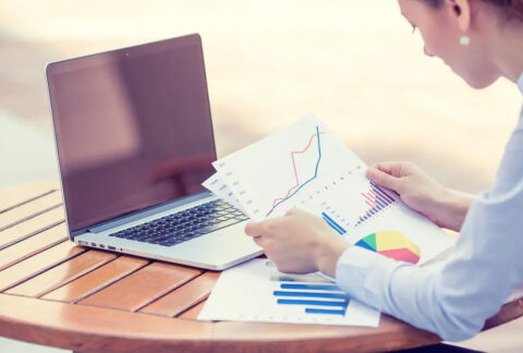 Businesswoman at table looking at printed cashflow graphs in front of open laptop