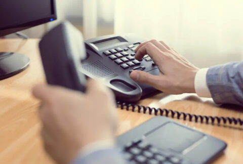 Businessman at desk holding phone receiver and dialing number in keypad