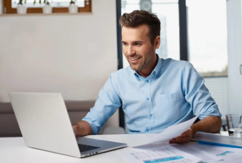 Businessman working on laptop and holding documents at desk