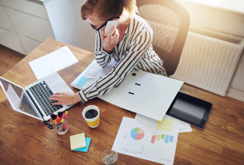 Businesswoman taking a phonecall while using laptop at desk