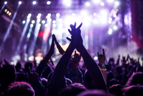 Audience with hands raised at concert with bright lights