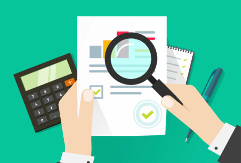 Cartoon of businessman's hands holding a tax document and a magnifying glass over it in front of calculator and notebook and pen