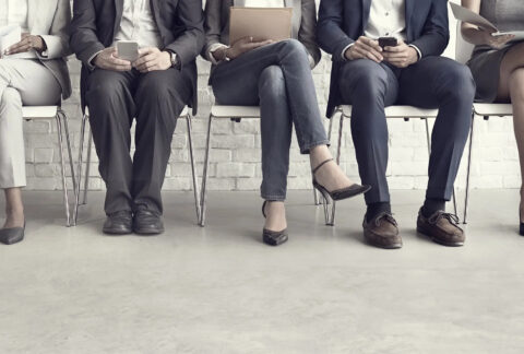 Bottom half of five interview candidates sitting on chairs in a row