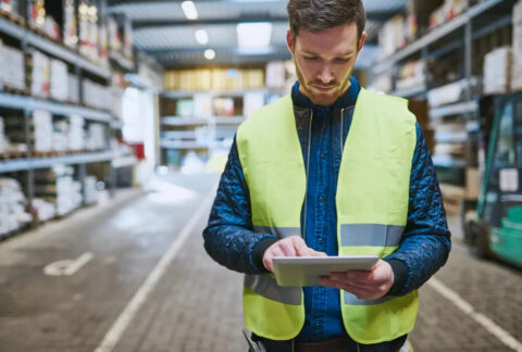 Warehouse worker in high-vis standing using tablet