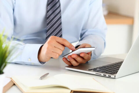Businessman using smartphone in front of open laptop
