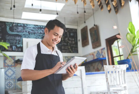 Small business owner standing in cafe using tablet and smiling