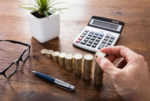 Hand making increasingly tall stacks of coins in front of calculator