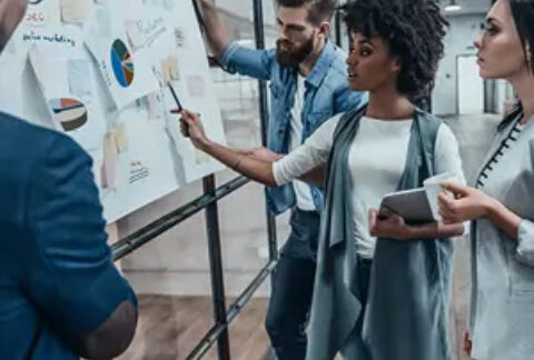 Businesspeople gathered around whiteboard in office with post-it notes and charts on it