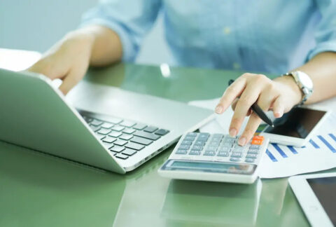 Businesswoman using calculator with one hand and laptop with the other
