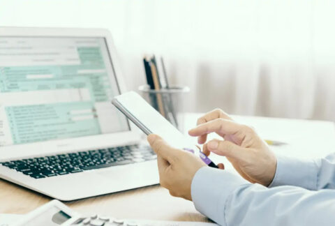 Businessman using smartphone at desk in front of open laptop