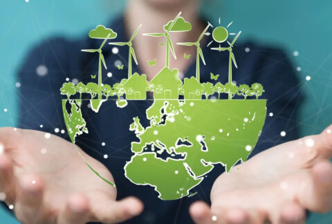Hands holding globe-shaped image with map of the world on bottom half and houses, trees, wind turbines and sky on top half