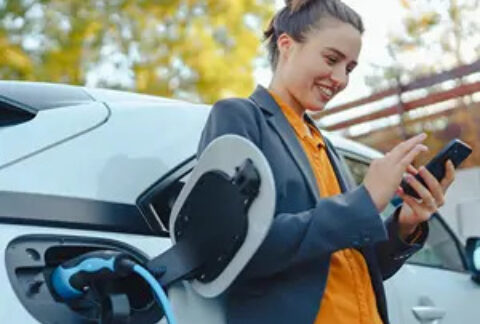 Woman using smartphone and smiling next to charging electric car